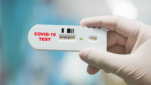 COVID Test Photo of a COVID test being held by a hand with a rubber glove on it. The result on the test is positive.