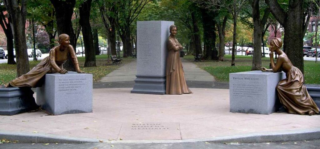 Boston Women’s Memorial A photo of the Boston Women's Memorial - three grey columns spread out across the entrance to a walkway at the Boston Common, each with a bronze statue of a notable women from Boston history leaning or sitting on it.