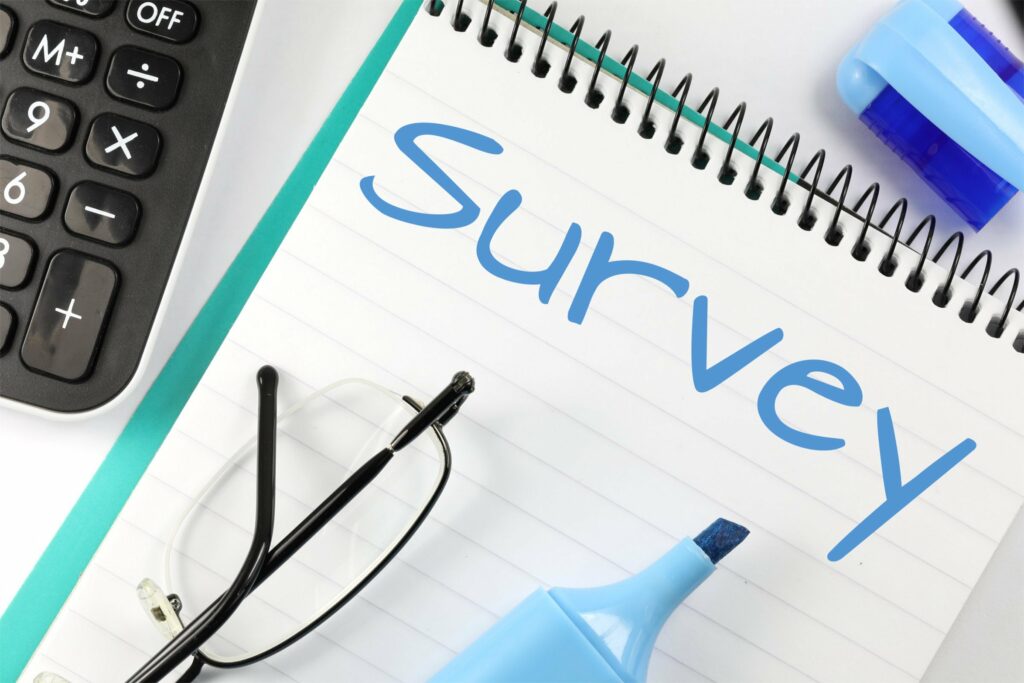 A picture of a notepad with survey written across the top together with a blue pen, calculator and glasses.