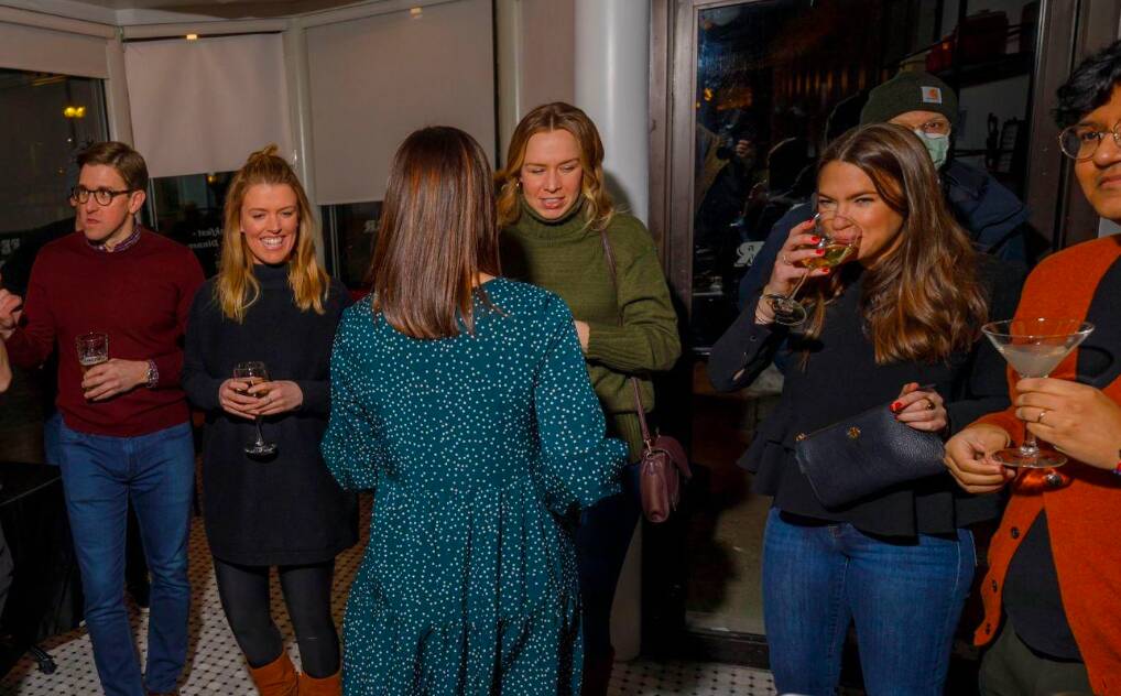 A group of young NABB members gathering at a local establishment, looking at each other and talking, with drinks in their hands